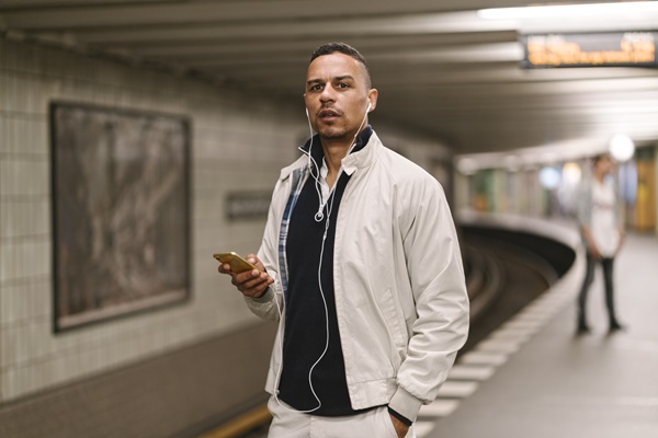 Man with headphones waiting on subway platform.