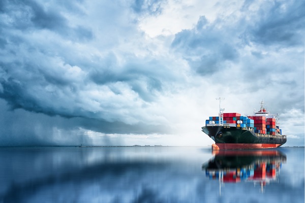 Cargo ship on reflective sea under stormy clouds.