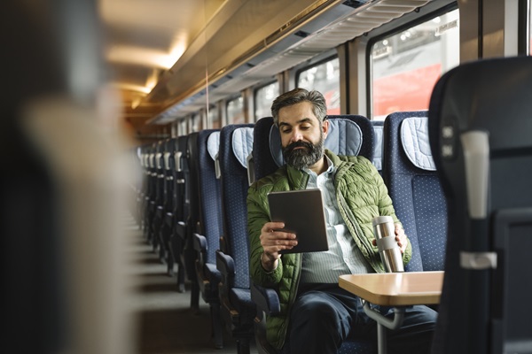 uomo seduto in treno che usa il tablet