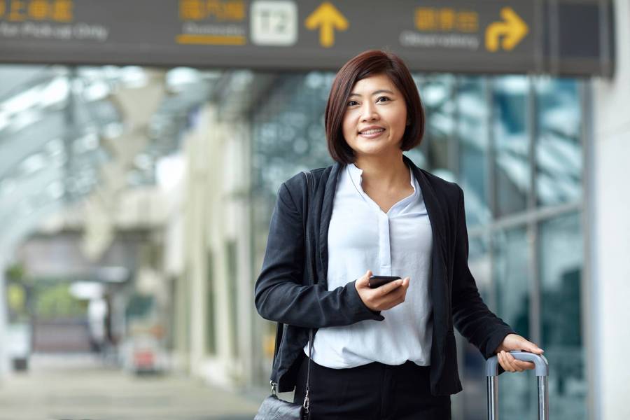 Smiling traveler with phone and suitcase in airport.