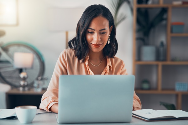 Woman smiling while working on laptop at desk.