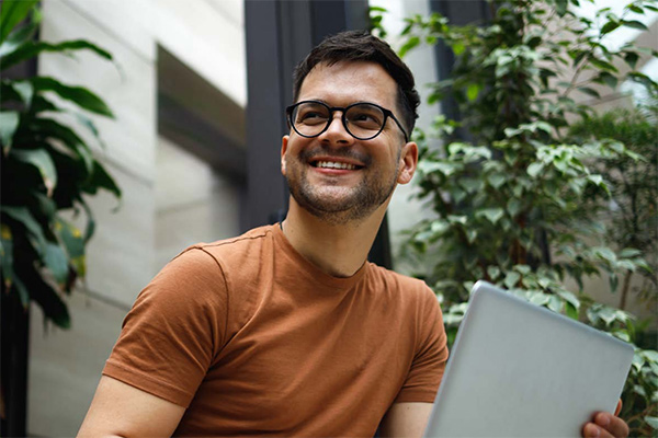 Smiling man with laptop sitting outdoors.